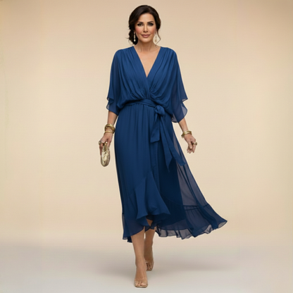 Model in the navy blue chiffon midi dress with draped V-neck, bow-tied waist and swirling ruffled hem, holding a gold clutch. 3