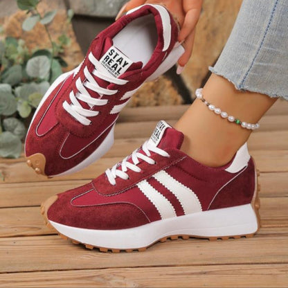 Burgundy suede trainers with white stripes and laces, worn with cuffed jeans on a wooden deck 4