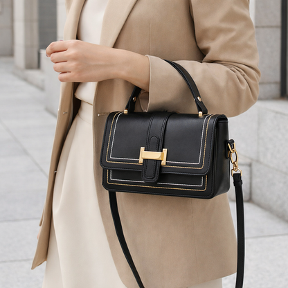 Model in a beige blazer carrying the black bag on her forearm by the top handle, gold clasp facing forward. 6