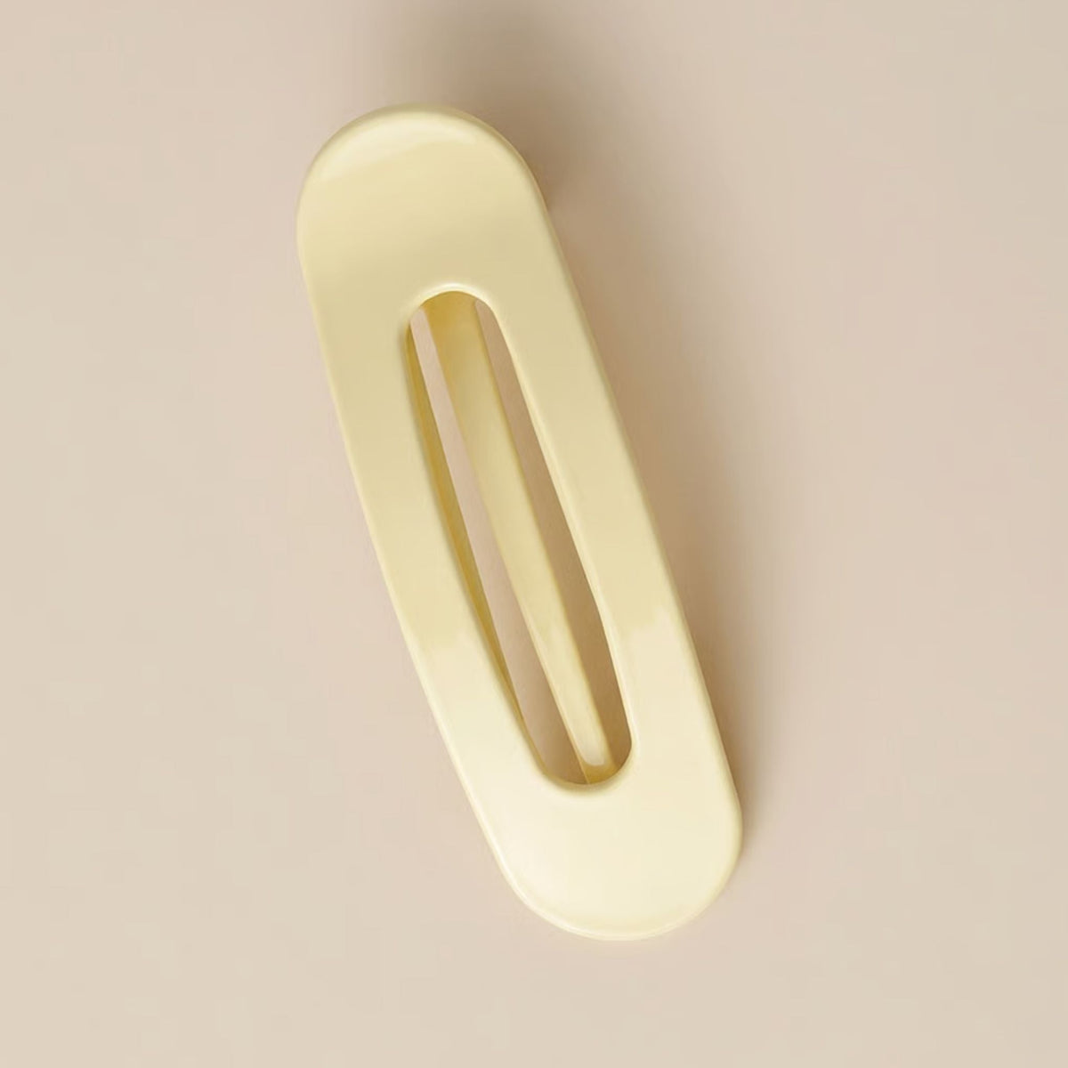 Glossy pale yellow flat clip with a long oval opening, photographed from above on a beige surface 6