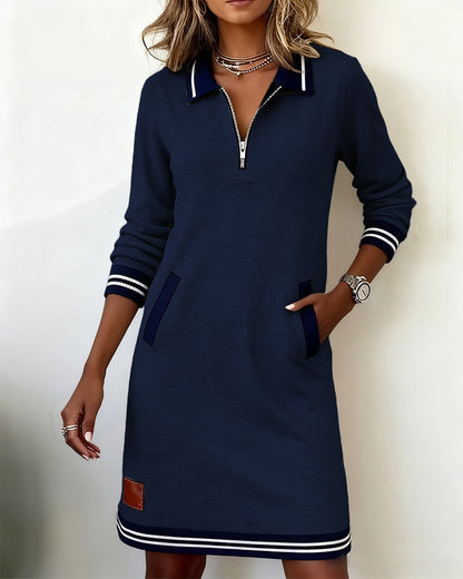 Navy blue dress from the front on a model, hand in pocket, with ribbed striped cuffs and hem. 17