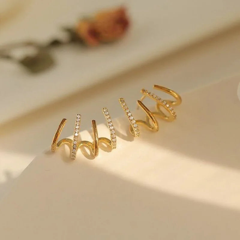 Gold pair on a cream surface with a dried flower blurred behind, showing the curved claw shape 8
