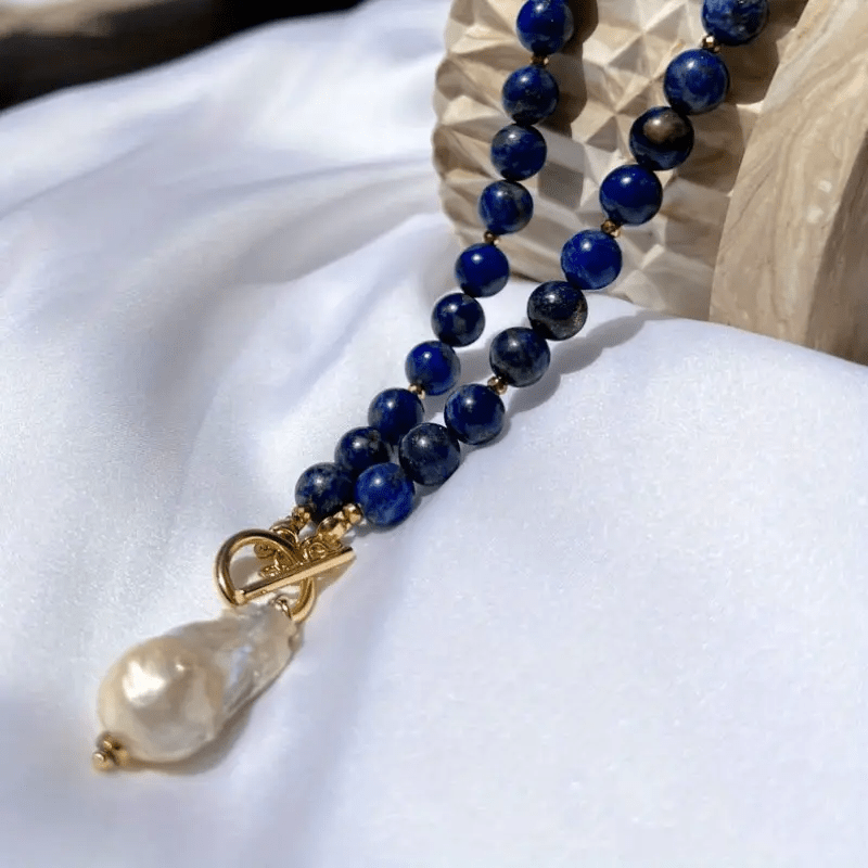 Necklace laid on white fabric beside a carved wooden block, with the pearl and gold toggle in front 6