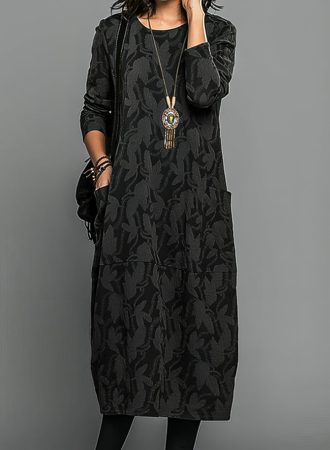 Model wearing the dress in black with a tonal leaf pattern, pendant necklace and black bag 4