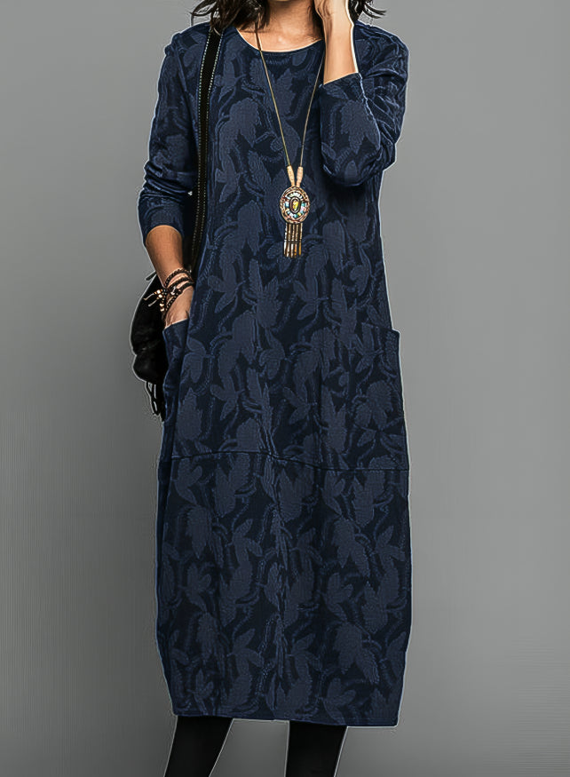 Model wearing the dress in navy blue with a tonal leaf pattern, pendant necklace and black bag 3