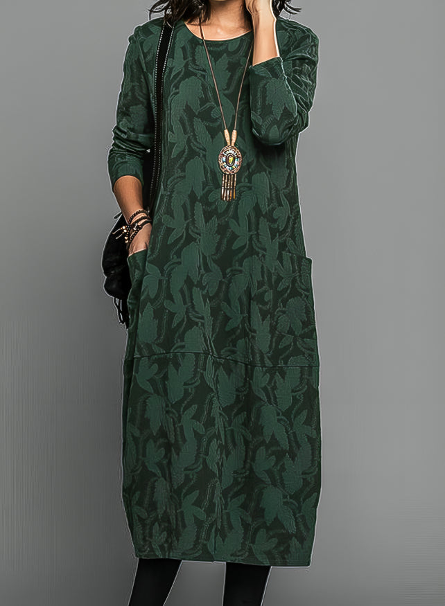 Model wearing the dress in dark green with a tonal leaf pattern, pendant necklace and black bag 1