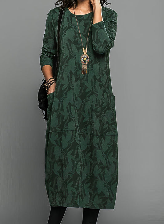 Model wearing the dress in dark green with a tonal leaf pattern, pendant necklace and black bag 1