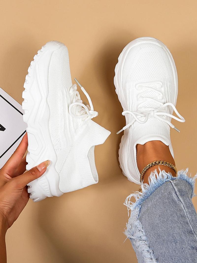 Top-down view of white knit sneakers with chunky soles, one held in a hand and one worn with frayed jeans. 9