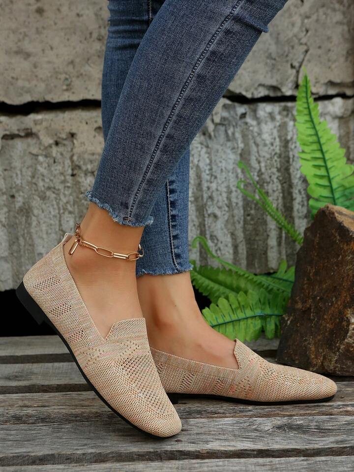Side view of beige knitted slip-ons with a flat black sole, worn with frayed jeans beside fern leaves. 4