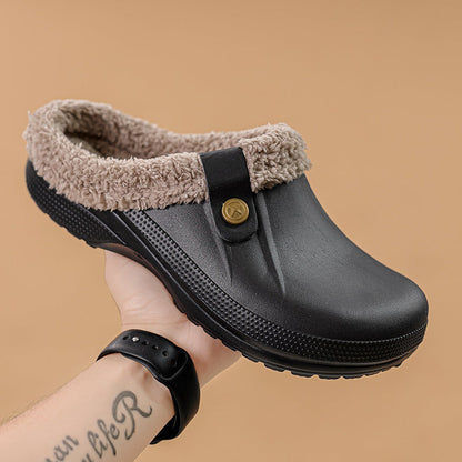 Hand holding a black clog with beige fleece collar and button strap against a tan background 2