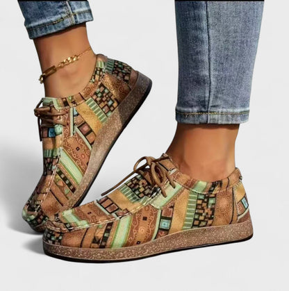 Model wearing earthy brown and sage green patterned lace-up shoes with a cork-style sole, with a gold chain anklet and jeans. 4