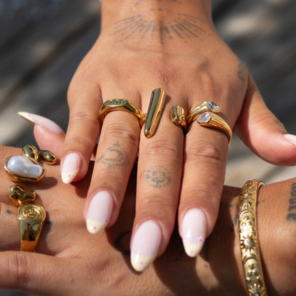 Top view of two hands in the sunlight, the bar ring on a finger alongside other gold rings and a patterned bangle. 4