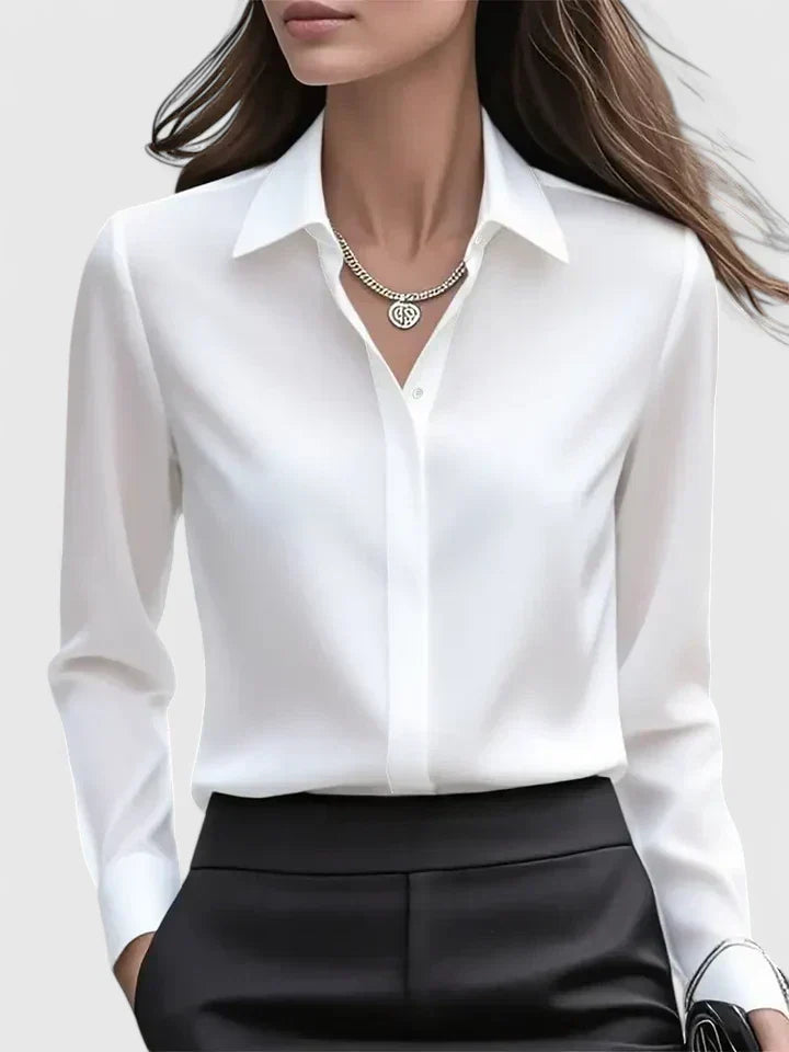 Front view of the white satin blouse on a model, with pointed collar and concealed button placket, tucked into black trousers. 2