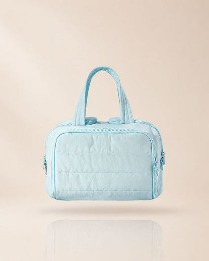 Light blue quilted organiser bag with two handles, front view on a soft beige background with a faint reflection. 13