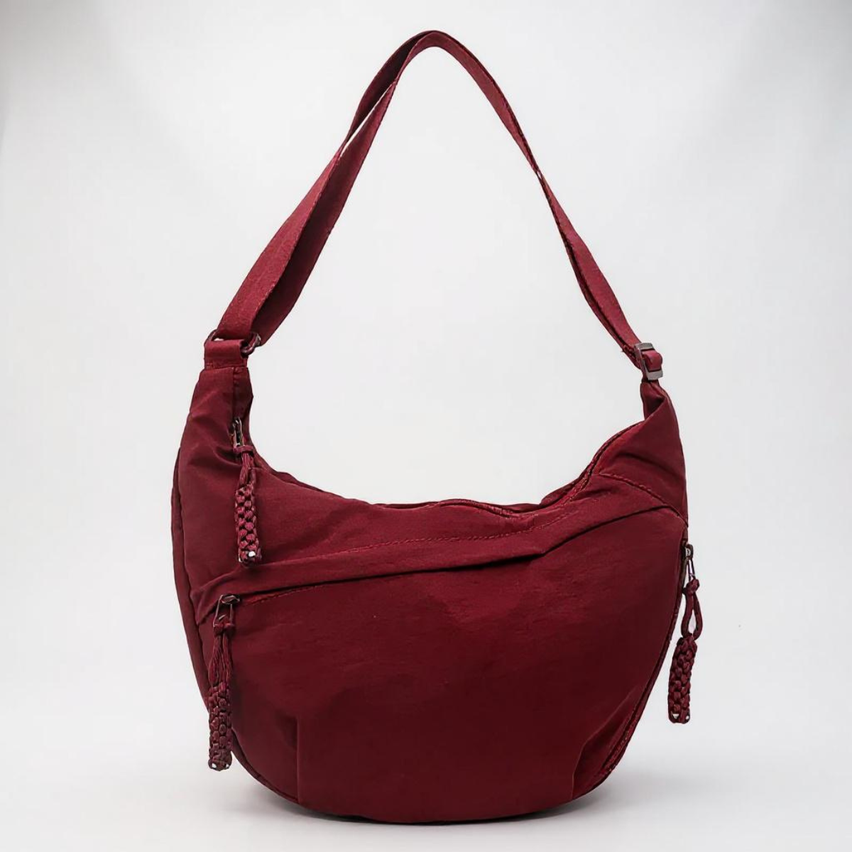 Burgundy half-moon bag on a plain backdrop, with a looped shoulder strap and braided zip pulls 1