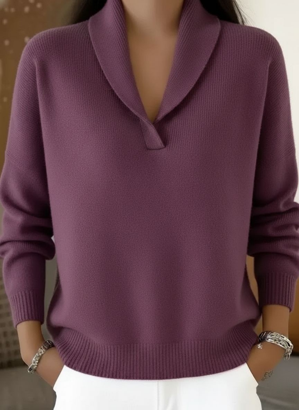 Knitted V-neck jumper in a muted plum purple, worn by a model with hands in the pockets of white trousers. 5
