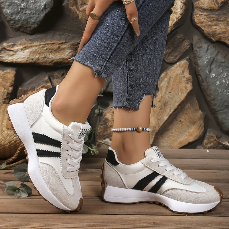 Cream and black trainers with black side stripes, worn with frayed jeans against a stone wall 5