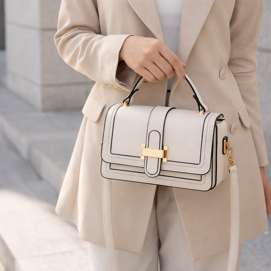 Model in a beige blazer carrying the cream bag by its top handle, with the gold clasp and detachable strap visible. 2