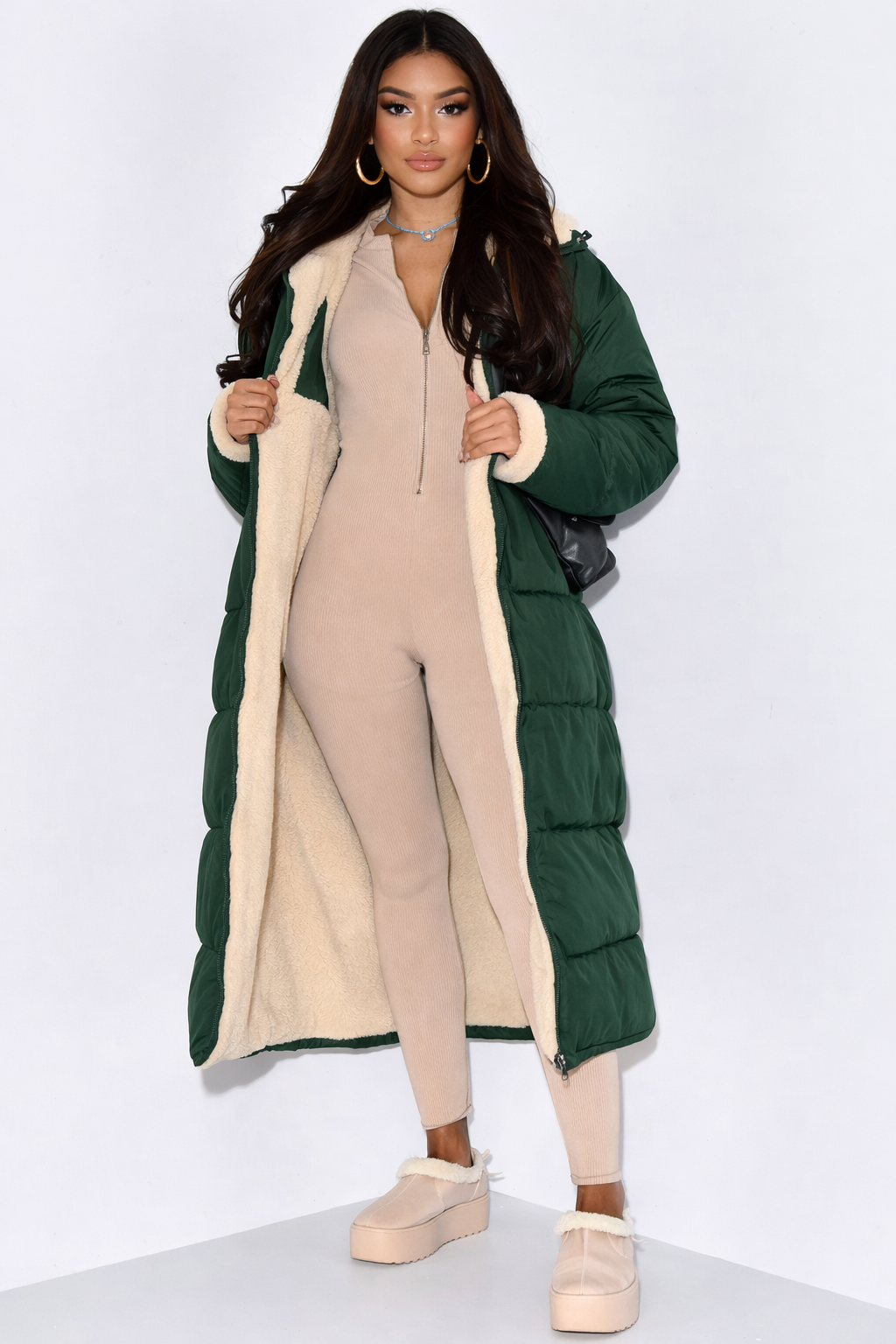 Model wears the dark green padded side open over a beige ribbed jumpsuit, showing the cream fleece lining and cuffs. 3