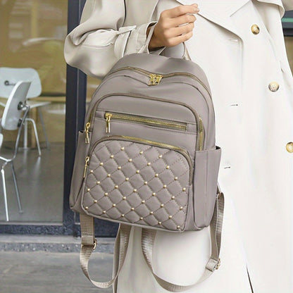 Taupe backpack held by its top handle against a cream coat, showing the studded quilted front pocket 5