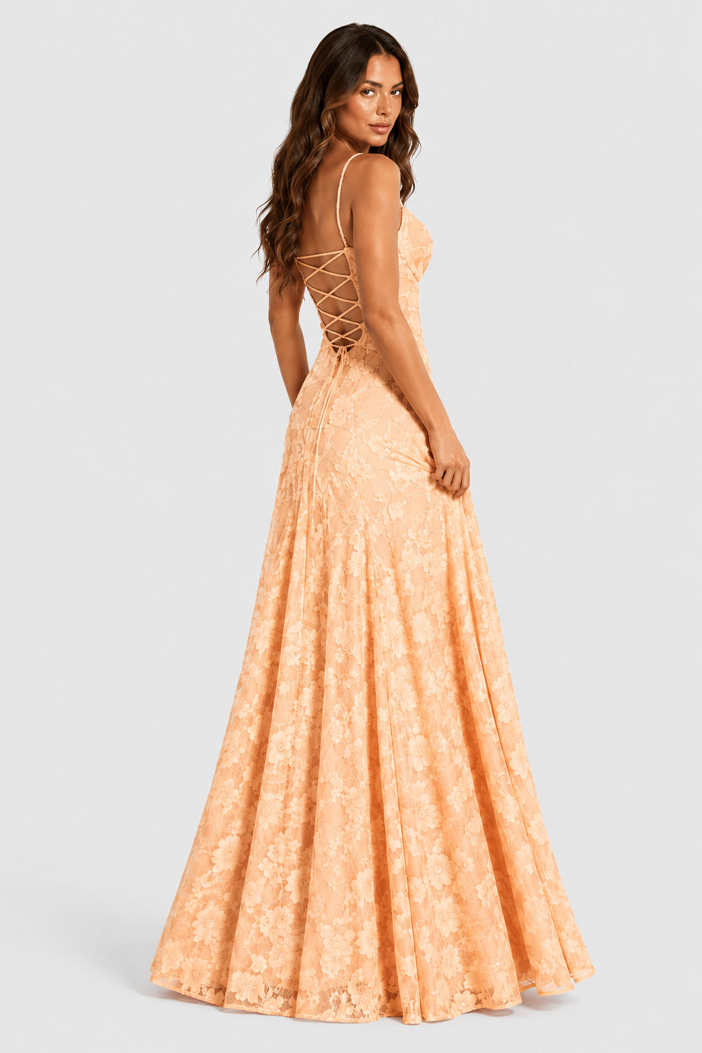 Peach lace gown from behind, model looking back over her shoulder to show the criss-cross lace-up back and flared skirt. 14