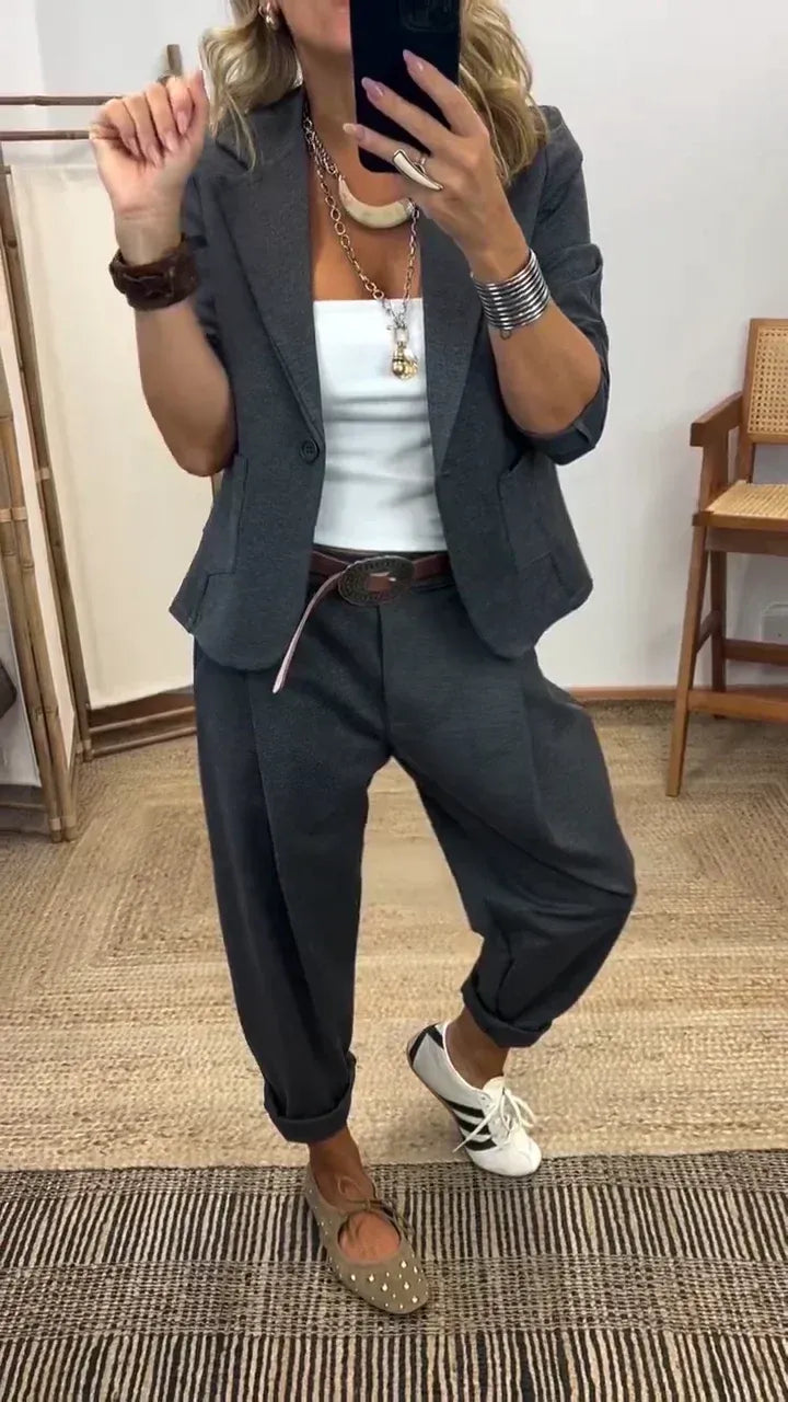 Woman in a dark grey single-button blazer and rolled-cuff trousers over a white top, photographed in a mirror selfie. 1