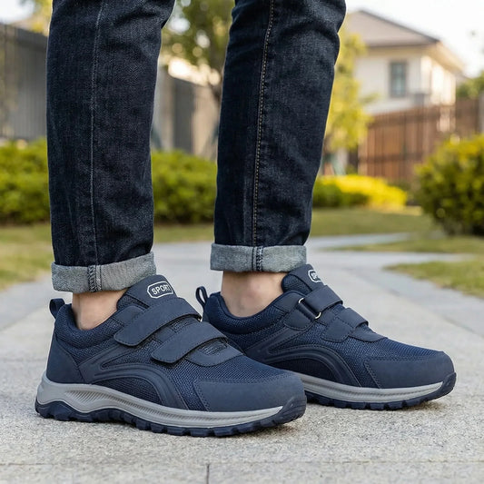 Navy walking shoes with two straps worn by a man in rolled dark jeans on a garden path 1