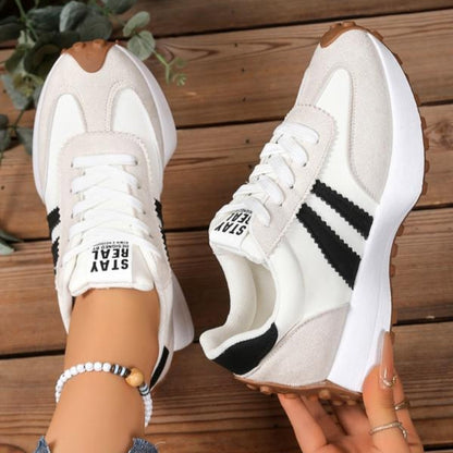 Cream suede trainers with black stripes and white laces, seen from above, one held in hand 10