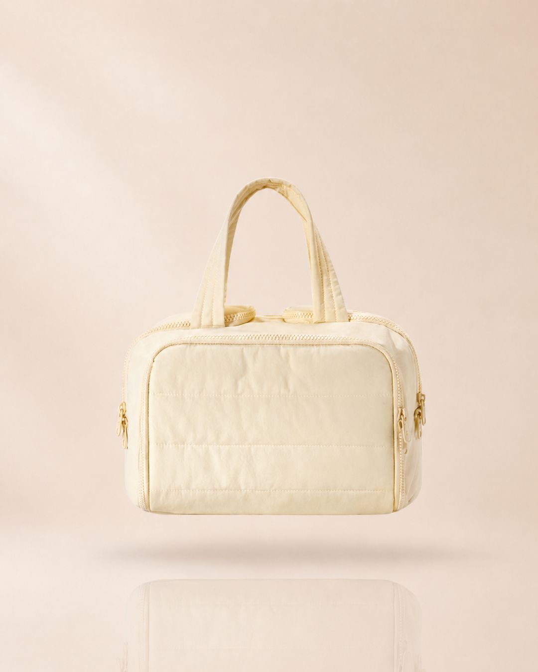 Cream quilted organiser bag with two handles, front view on a soft beige background with a faint reflection. 14