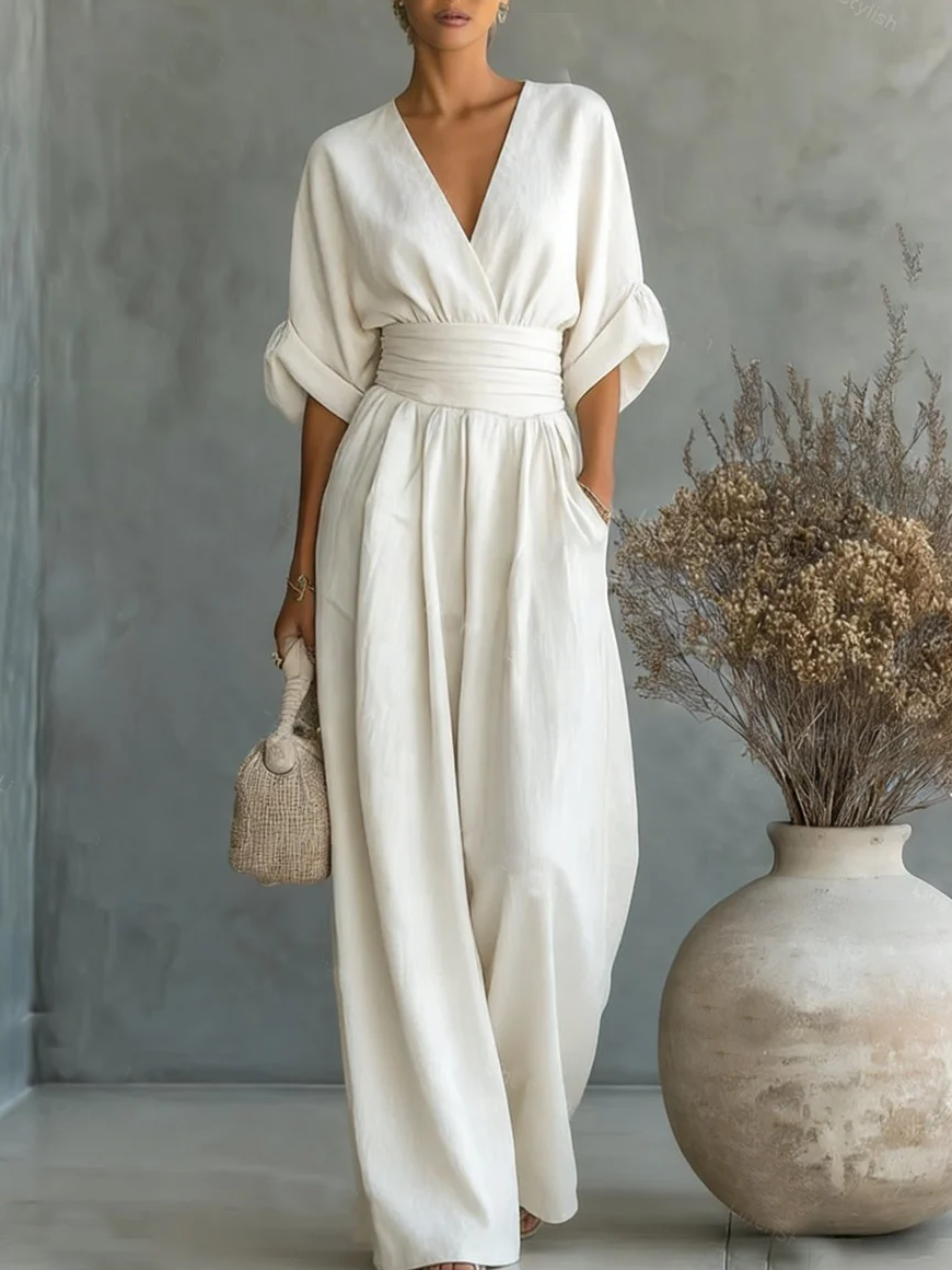 Model in the cream jumpsuit with a hand in the pocket, holding a woven bag beside a large vase 1