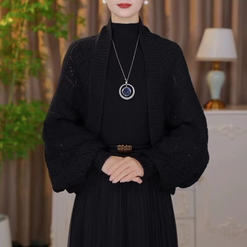 Model wearing the open knit shawl cardigan in black over a black high-neck top and pleated skirt 3