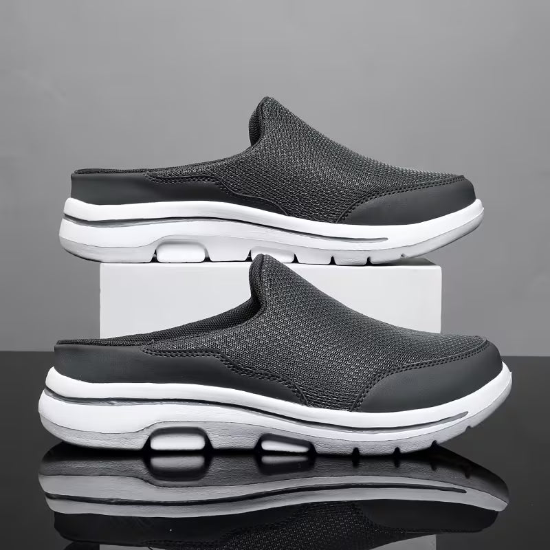 Pair of dark grey mesh backless slip-ons with white soles, one stacked on a white block against a grey backdrop. 2
