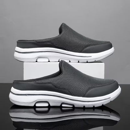 Pair of dark grey mesh backless slip-ons with white soles, one stacked on a white block against a grey backdrop. 2