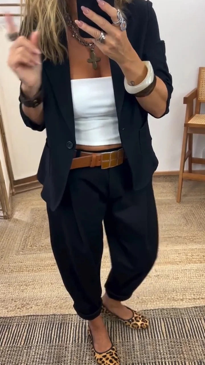 Woman in the black blazer and black trousers with rolled hems, worn with a white top and a tan leather belt. 3