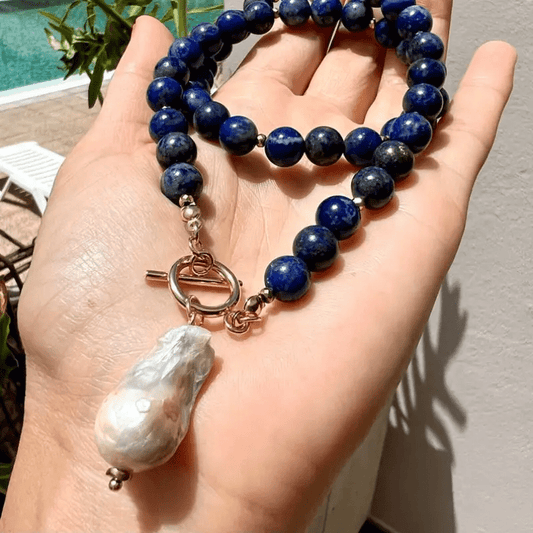 Necklace resting in an open palm outdoors, showing the deep blue beads and large baroque pearl 2