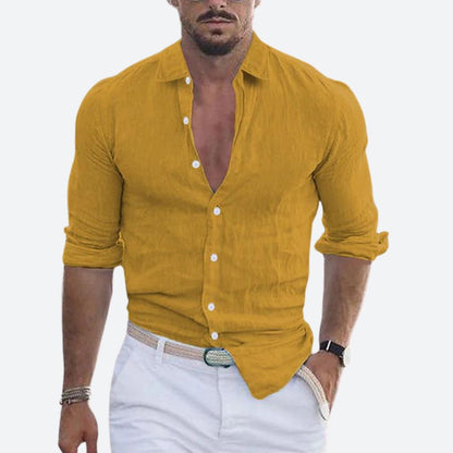 Man wearing the shirt in mustard yellow, open at the collar with sleeves rolled, styled with white trousers and a woven belt. 2