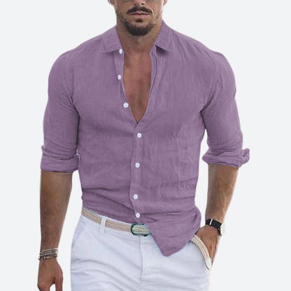 Man wearing the shirt in soft lilac purple, open at the collar with sleeves rolled, styled with white trousers and a woven belt. 9