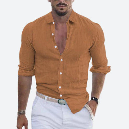 Man wearing the shirt in caramel brown, open at the collar with sleeves rolled, styled with white trousers and a woven belt. 3