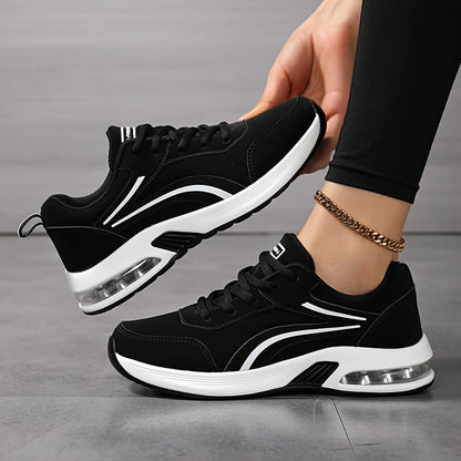 Black lace-up trainers with white stripes and clear air-cushion soles, one shoe held up by a hand 1