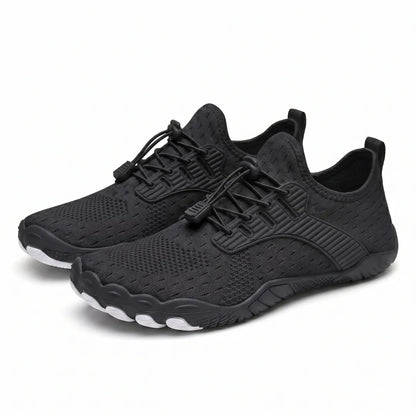Pair of black knit barefoot trainers seen at an angle, with toggle laces, ridged overlays and white toe-shaped sole tips. 43