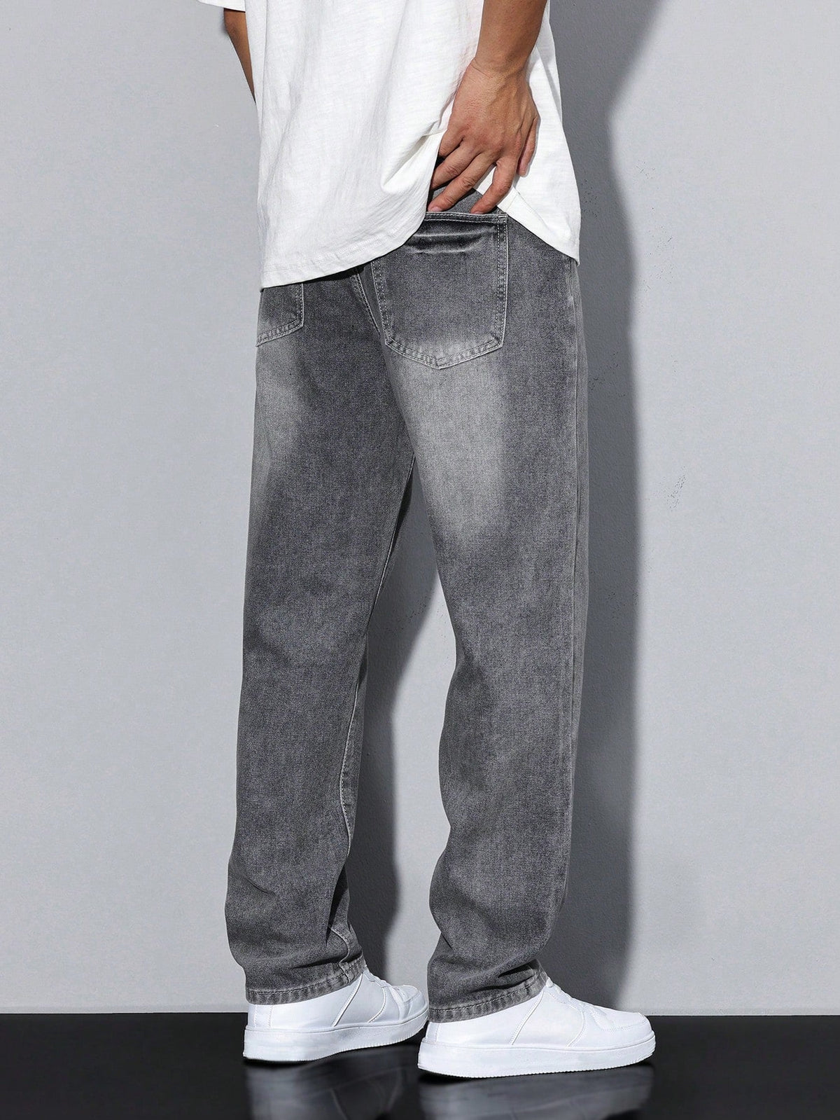 Back view of washed grey jeans showing the patch back pockets and straight leg, worn with white trainers. 4