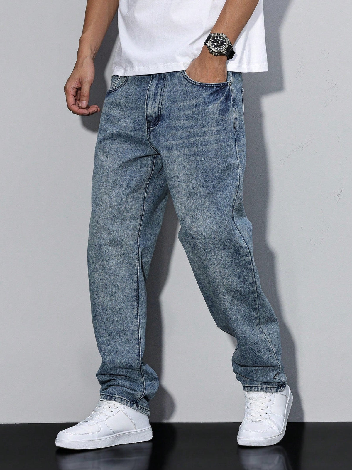 Mid-blue washed baggy jeans on a model in a walking pose, hand in pocket, with white tee and trainers. 6