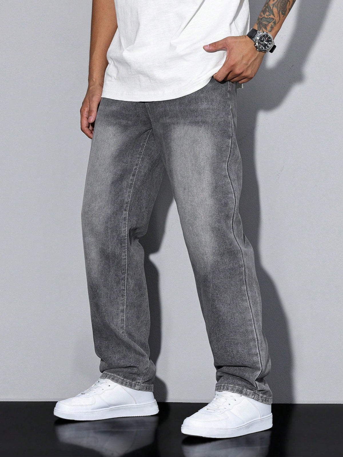 Side view of washed grey loose-fit denim jeans worn by a model with a white tee and white trainers, hand in pocket. 1