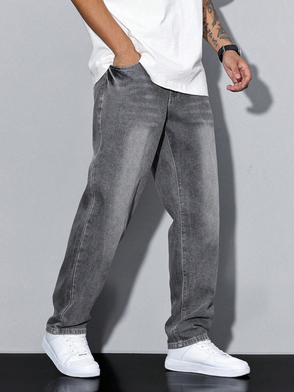 Model walking in grey washed baggy jeans, seen from the left side with a hand in the pocket and white trainers. 3