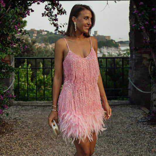 Smiling model in pink fringed sequin mini dress with feather hem, holding a clutch outdoors 1
