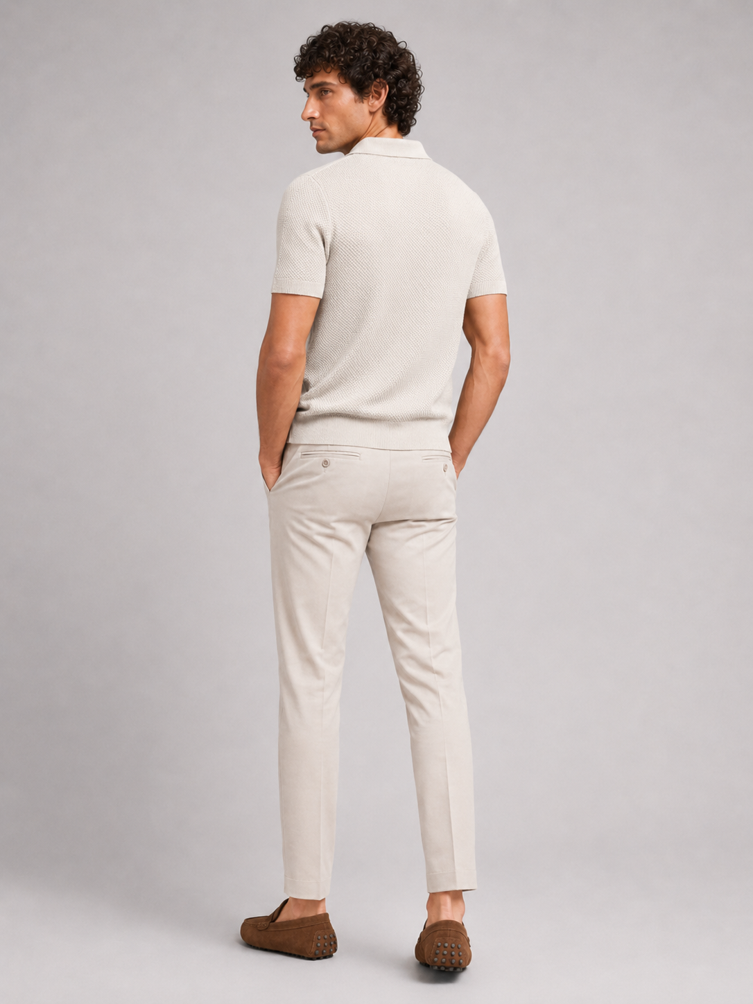Back view of model in off-white knit polo with beige trousers and brown driving loafers 19