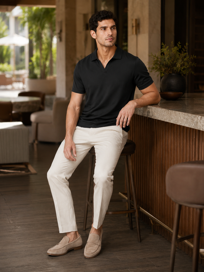 Model in the black polo seated on a bar stool in a stylish lounge, wearing cream trousers and suede loafers. 10