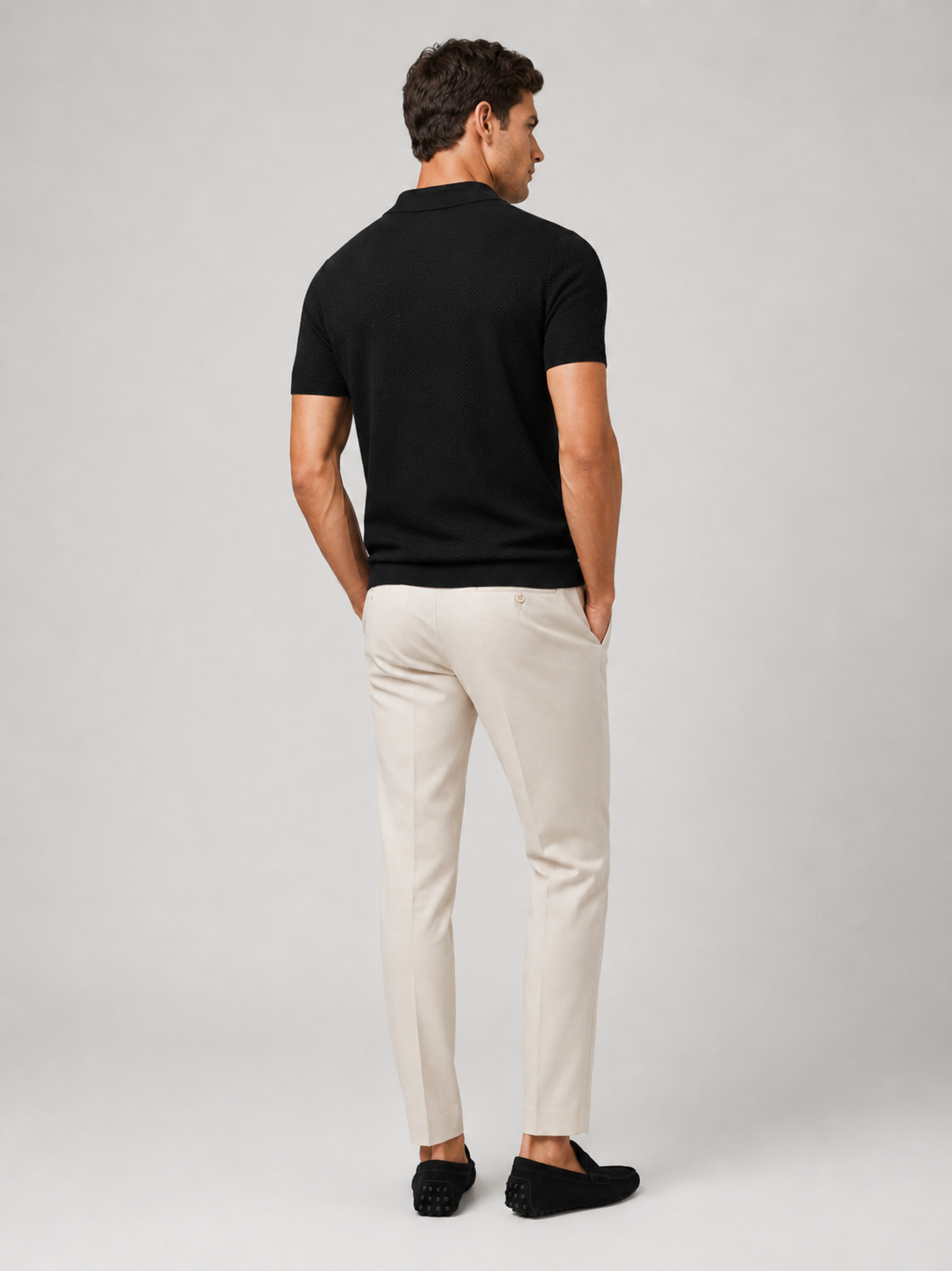 Back view of model in black knit polo with cream trousers and black driving loafers 9