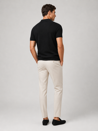 Back view of model in black knit polo with cream trousers and black driving loafers 9