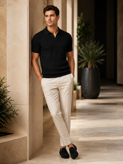 Model in black knit polo leaning against a stone wall in a sunlit colonnade 10